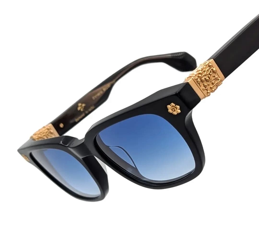 Gazal-brand sunglasses in black acetate with sculptural gold coral-motif hardware, angled macro product shot on white